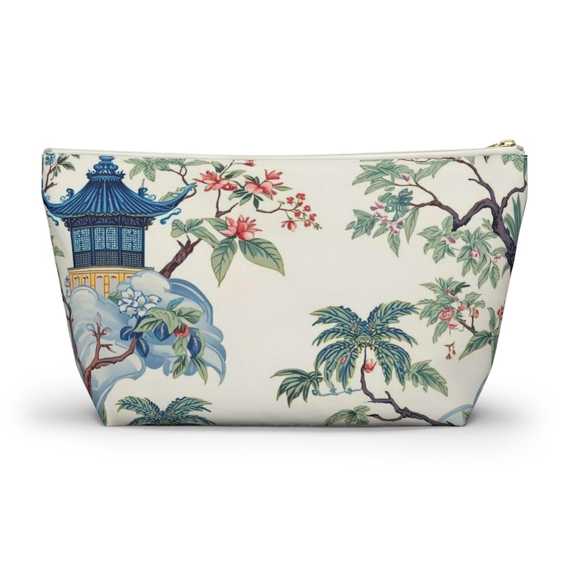 K&ouml;nnte beinhalten: Eine Rei&szlig;verschlusstasche mit cremefarbenem Hintergrund und einem Druckmuster aus einer blauen Pagode, gr&uuml;nen Palmen und rosafarbenen bl&uuml;henden Zweigen. Das Design zeigt detaillierte Illustrationen von B&auml;umen und Blattwerk auf der gesamten Oberfl&auml;che.