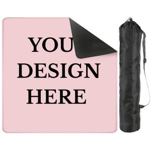 May include: A light pink rectangular mat with the words "YOU DESIGN HERE" in black. A portion of the mat is folded over, revealing a black underside. A black carrying bag with a shoulder strap is to the right.