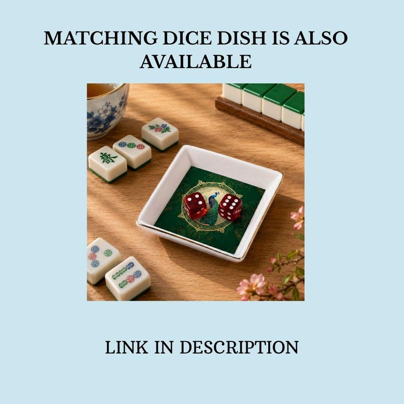 Puede incluir: Un plato cuadrado de cer&aacute;mica blanca con borde dorado que presenta un gr&aacute;fico de pavo real verde en el centro, conteniendo dos dados rojos transl&uacute;cidos. El texto MATCHING DICE DISH IS ALSO AVAILABLE y LINK IN DESCRIPTION es visible.