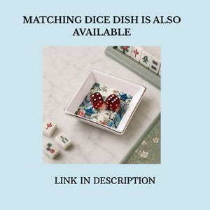 May include: A square white ceramic dish with a gold-toned rim, featuring a colorful floral and pagoda pattern on the interior base. Two translucent red dice with white pips rest inside the dish. Text reads: MATCHING DICE DISH IS ALSO AVAILABLE. LINK IN DESCRIPTION.