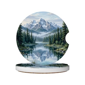 May include: Round car coaster featuring a scenic landscape with a snow-capped mountain range, a calm lake, and evergreen trees. The artwork is a watercolor painting with soft blues, greens, and whites. The coaster has a white rim and a natural wood base.