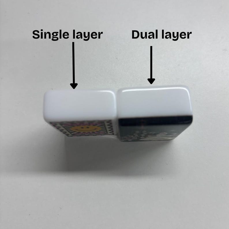 Puede incluir: Dos fichas rectangulares con lados blancos y reverso negro, colocadas una al lado de la otra. La ficha izquierda est&aacute; etiquetada como Single layer con una flecha, y la derecha como Dual layer con una flecha. La ficha izquierda tiene un sol amarillo.
