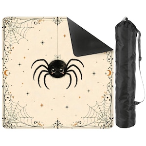 May include: A square outdoor blanket with a cream-colored top featuring a central black spider illustration, spiderwebs in the corners, and small star accents. The blanket has a black underside and comes with a black drawstring carrying bag.