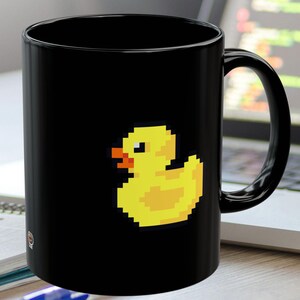 May include: A black ceramic mug featuring a yellow pixelated rubber ducky design.