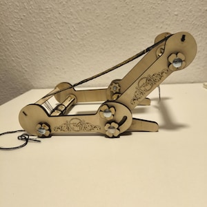 Puede incluir: Un telar de madera con una cuerda negra enhebrada. El telar tiene un diseño floral y detalles metálicos plateados.