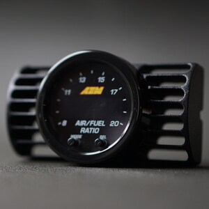 Puede incluir: Un medidor de relaci&oacute;n aire/combustible negro con una pantalla digital, con el texto "AIR/FUEL RATIO" y el logotipo de la marca "AEM". El medidor est&aacute; montado en una carcasa negra con un dise&ntilde;o ranurado.