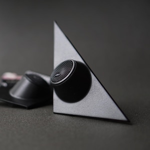 Puede incluir: Un juego de altavoces de audio para coche. Un altavoz está montado en un panel triangular plateado. El altavoz es negro con una rejilla de malla y un borde plateado. Otro altavoz y un panel están en el fondo.