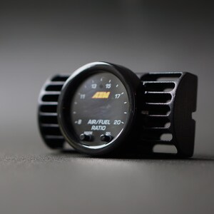 Puede incluir: Medidor de relaci&oacute;n aire/combustible AEM negro con pantalla circular y carcasa negra. El medidor tiene una aguja y n&uacute;meros que indican la relaci&oacute;n aire/combustible. Dise&ntilde;ado para uso automotriz.