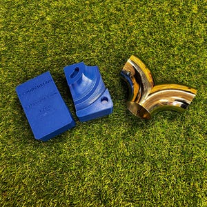 Puede incluir: Un objeto rectangular azul con texto y un objeto curvo azul junto a un objeto curvo brillante de color dorado. El objeto azul tiene el texto "#coupcustom" y medidas. Los objetos están sobre una superficie verde.
