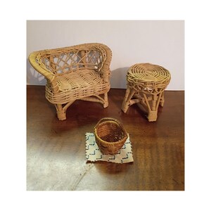 May include: A miniature dollhouse furniture set consisting of a light brown woven wicker armchair and a matching round wicker stool. A small brown woven basket sits on a square piece of white fabric with a blue stitched pattern in the foreground.