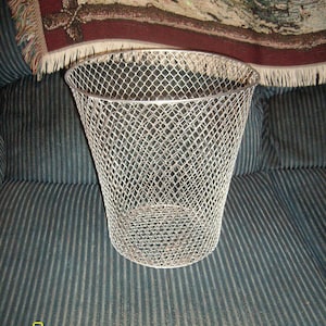 May include: A silver wire mesh trash can with a conical shape. The can is sitting on a striped fabric surface.