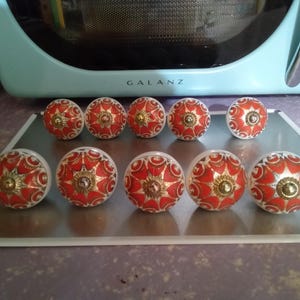 May include: Ten ceramic drawer knobs with a white background and red and gold floral design.