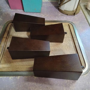 May include: Four dark brown wooden furniture legs with a slightly rounded top and a metal screw on the bottom.