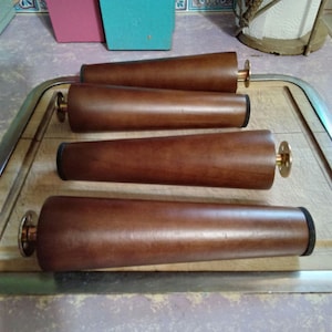 May include: Four wooden furniture legs with brass accents. The legs are brown and have a smooth finish. They are arranged on a silver tray.