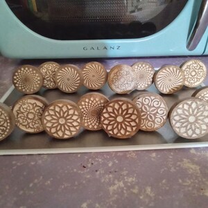 May include: A collection of 13 wooden coasters with intricate laser-cut designs. The coasters are circular and feature a variety of patterns, including swirls, geometric shapes, and floral motifs. The coasters are all made of natural wood and have a light brown color.