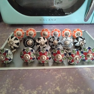 May include: A collection of 15 ceramic drawer knobs with various floral patterns in shades of blue, red, white, and black. The knobs have a silver metal base.