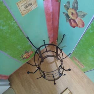 May include: A dark brown metal mug tree with a circular base and multiple curved hooks extending outward. The stand features a tiered design with two rings connected by vertical supports, providing a structured frame for hanging various items.