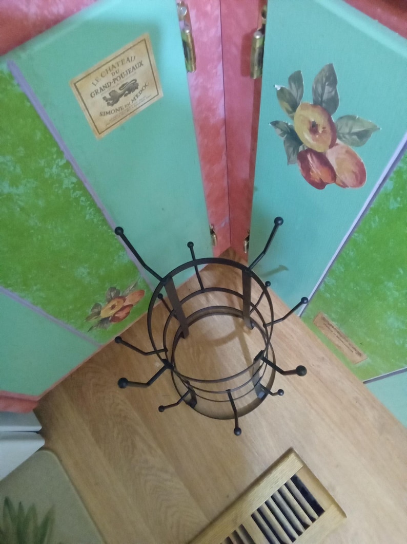 May include: A dark brown metal mug tree with a circular base and multiple curved hooks extending outward. The stand features a tiered design with two rings connected by vertical supports, providing a structured frame for hanging various items.