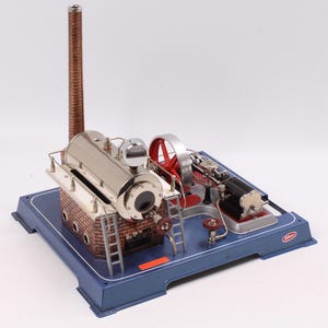 Puede incluir: Un detallado modelo de máquina de vapor con una caldera plateada brillante, un volante rojo y una chimenea de ladrillo. El motor se asienta sobre una base azul con ribete plateado. Incluye pequeñas escaleras y varios componentes mecánicos.