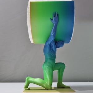 May include: A 3D printed sculpture of a person kneeling and holding a large, green, blue, and yellow gradient cylinder above their head.