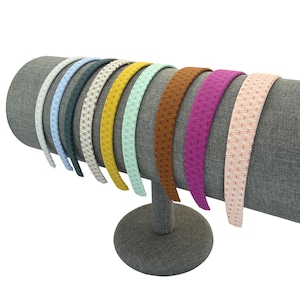 May include: A display of colorful headbands with various geometric patterns. The headbands are in shades of gray, blue, green, yellow, brown, purple, and pink. They are arranged on a gray cylindrical display stand.