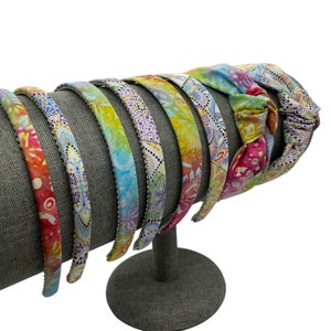 May include: A set of colorful patterned headbands with a tie-dye design. The headbands are displayed on a gray stand.
