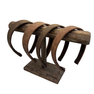 May include: A display of five brown headbands on a wooden stand. The headbands have a suede-like texture and vary in shades of brown. The stand is made of weathered wood, adding a rustic touch to the presentation. The headbands are evenly spaced.