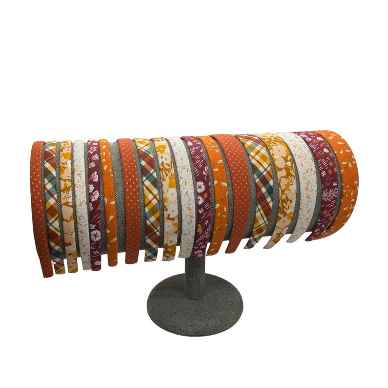 May include: A display of colorful patterned headbands in shades of orange, red, and white. The headbands are arranged in a circle on a gray stand.