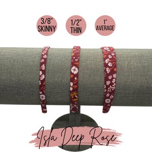May include: Three red headbands with a floral print in different widths: 3/8 inch skinny, 1/2 inch thin, and 1 inch average. The headbands are displayed on a gray stand. The text "Isla Deep Rose" is written below the stand.