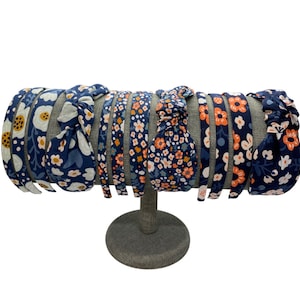 May include: A display of eight blue and orange floral print headbands with knotted ends. The headbands are displayed on a gray stand.