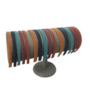 May include: A collection of fourteen thin headbands arranged on a cylindrical display stand. Each headband features a textured, honeycomb-like pattern and comes in a variety of colors including orange, dark blue, teal, maroon, and rust brown.