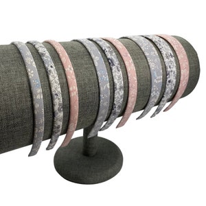 May include: A set of 10 floral patterned headbands displayed on a gray headband stand. The headbands are in shades of pink, gray, and white.
