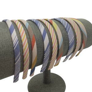 May include: A set of 10 colorful striped headbands displayed on a gray fabric headband stand. The headbands are made of fabric and have a variety of colors and patterns.