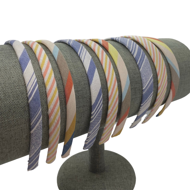 May include: A set of 10 colorful striped headbands displayed on a gray fabric headband stand. The headbands are made of fabric and have a variety of colors and patterns.