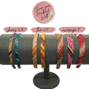 May include: Three fabric headbands in different widths: skinny (3/8 inch), thin (1/2 inch), and average (1 inch). The headbands are displayed on a gray stand and feature a colorful geometric pattern.