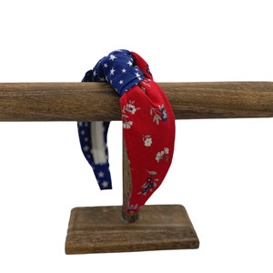 May include: A red and blue patterned headband with a knotted design. The headband is displayed on a wooden stand.