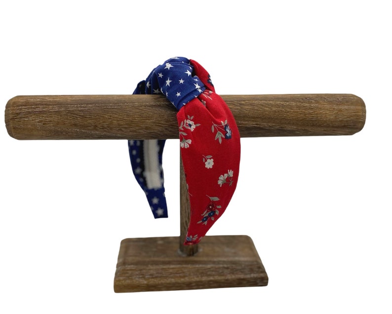 May include: A red and blue patterned headband with a knotted design. The headband is displayed on a wooden stand.