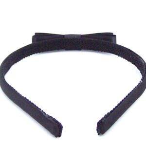 May include: A black headband with a black velvet bow. The headband is made of a soft, stretchy material.