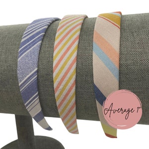 May include: Three fabric headbands with different striped patterns. The headbands are displayed on a gray fabric stand. The headband on the right has the text "Average 1" printed on it.