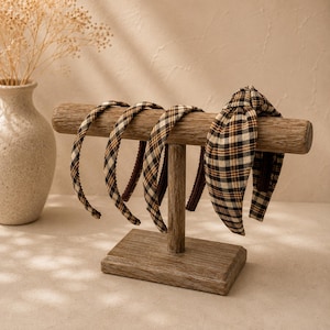 Peut inclure: Trois serre-têtes fins et un serre-tête large à nœud, tous dotés d'un motif à carreaux marron, noir et blanc. Les serre-têtes sont présentés sur un support en bois en forme de T avec une barre horizontale et une base rectangulaire.