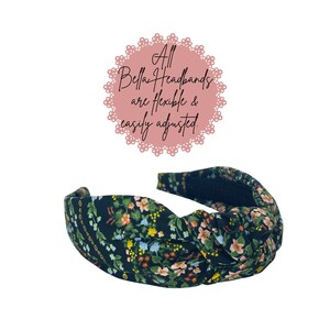 May include: A black floral headband with a knotted design. The headband features a pattern of small flowers in shades of pink, yellow, and green. Text above the headband reads "All Bella Headbands are flexible & easily adjusted."