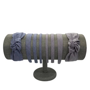 May include: A display of eight blue and purple fabric headbands on a gray stand. The headbands are made of a soft, textured fabric and have a knotted design.