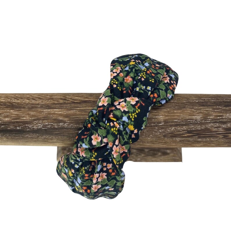 May include: A floral print headband with a dark background and a pattern of pink, yellow, and blue flowers. The headband is knotted and rests on a wooden surface.