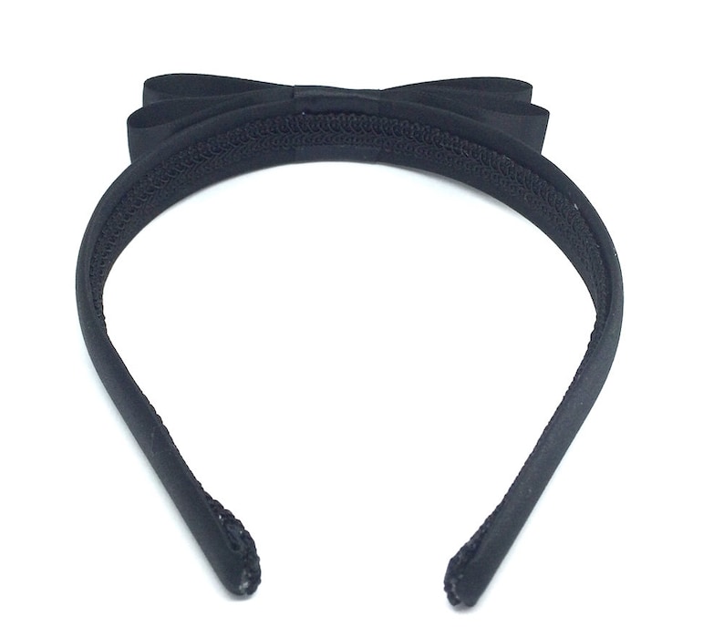 May include: Black headband with a large black satin bow. The headband is made of a soft, stretchy material.