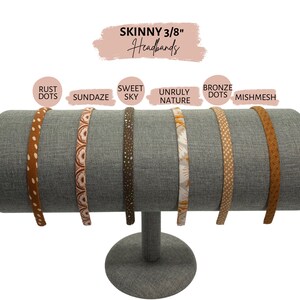 Op de afbeelding: Zes verschillende gepatroneerde haarbanden die op een grijze standaard worden getoond. De haarbanden zijn 3/8 inch breed en hebben patronen zoals roest stippen, Sundaze, Sweet Sky, Unruly Nature, bronzen stippen en mishmesh.