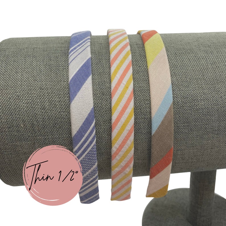 May include: Three striped fabric headbands, each 1/2 inch wide. The headbands are blue and white, orange and yellow, and pink and brown.