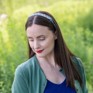 Peut inclure: Un serre-t&ecirc;te &agrave; motifs floraux avec un fond bleu et des fleurs blanches et vertes. Le serre-t&ecirc;te est port&eacute; sur la t&ecirc;te. La personne porte un haut bleu et un cardigan vert.