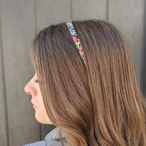 Peut inclure: Un serre-t&ecirc;te floral avec un fond noir est port&eacute; sur des cheveux bruns. Le serre-t&ecirc;te pr&eacute;sente de petites fleurs roses, bleues et vertes. Les cheveux sont longs et raides, avec une l&eacute;g&egrave;re ondulation aux extr&eacute;mit&eacute;s. La personne porte un blazer gris.