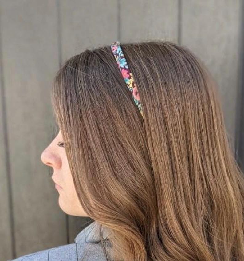Peut inclure: Un serre-t&ecirc;te floral avec un fond noir est port&eacute; sur des cheveux bruns. Le serre-t&ecirc;te pr&eacute;sente de petites fleurs roses, bleues et vertes. Les cheveux sont longs et raides, avec une l&eacute;g&egrave;re ondulation aux extr&eacute;mit&eacute;s. La personne porte un blazer gris.
