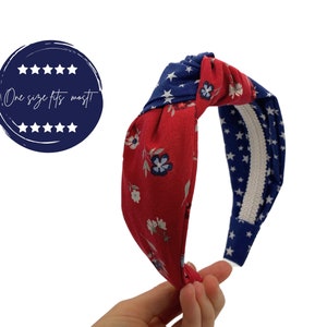 May include: Red and blue knotted headband with a floral pattern on one side and a white star pattern on the other side. "One size fits most" is written on a blue circle with white stars.